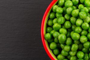 red-rimmed-bowl-of-green-peas-against-black-background